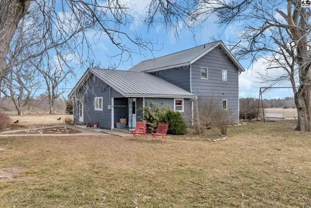 Gray farmhouse with a metal roof, white trim, and two red chairs on the porch.