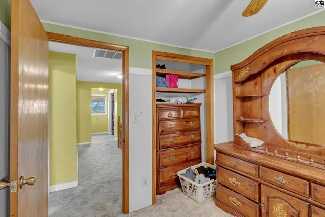 Bedroom with light green walls, a wooden dresser, and an open closet with shelves.