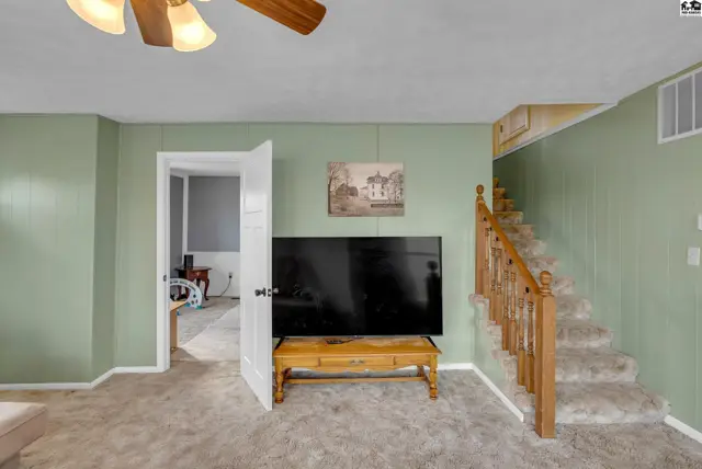 Living room with green paneled walls, plush carpet, and a wooden staircase leading upstairs.