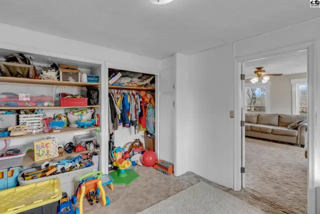 Bedroom with open shelves filled with toys and a closet with hanging clothes, opening to a living room.