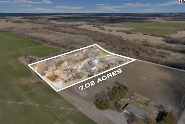 Aerial view of 7.02 acres featuring a cluster of buildings surrounded by trees and open fields.