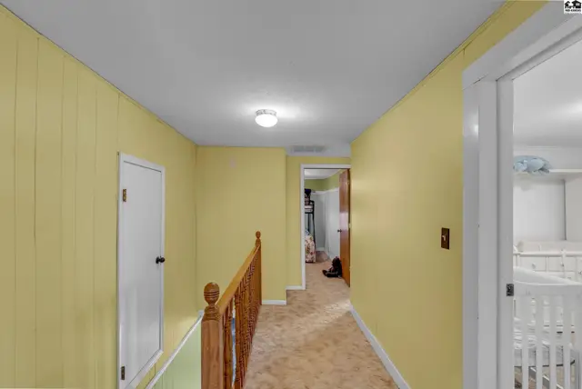 Hallway with yellow paneled walls, carpeted floor, and wooden banister leading to rooms.