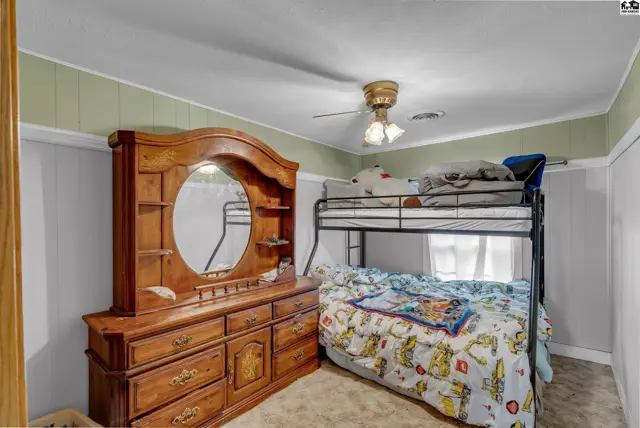 Bedroom with a wooden dresser, large mirror, and a black metal bunk bed with patterned bedding.