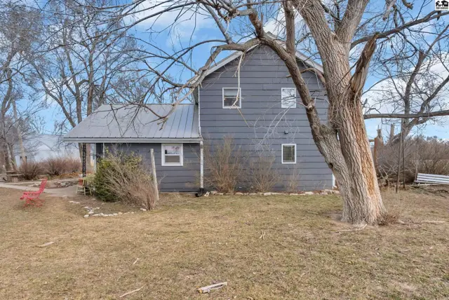 Gray clapboard house with a metal roof and mature trees in a grassy yard.