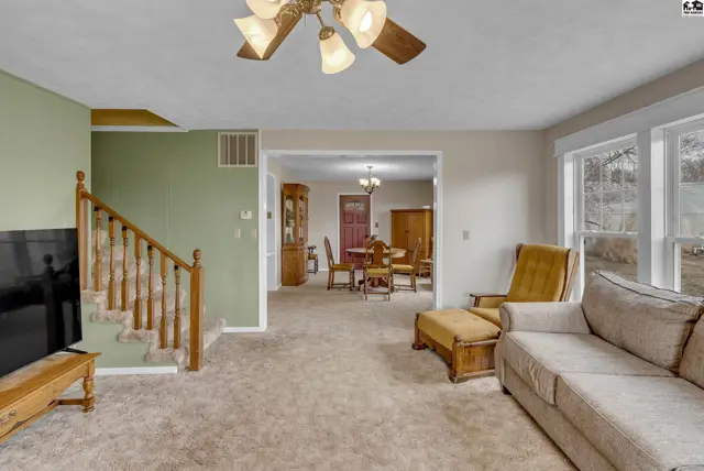 Spacious living room with plush carpet, wood-accented staircase, and view into dining area.
