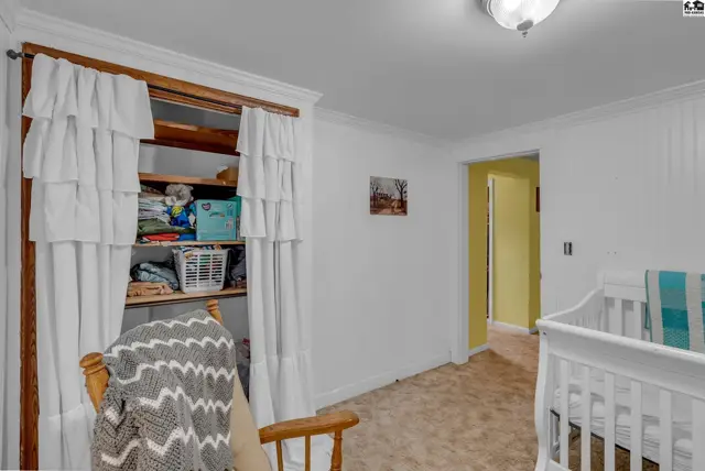 Nursery with white crib, wooden rocking chair, and open closet with ruffled curtains.