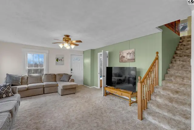 Spacious living room with plush carpet, sectional sofa, and light green accent wall leading to stairs.