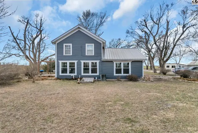 Blue clapboard farmhouse with white trim and a metal roof sits on a grassy lot.