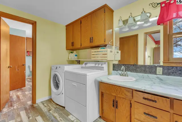 Spacious laundry room with wood cabinets, white appliances, and a marble countertop vanity.