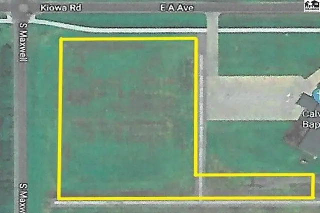 Aerial view of a vacant lot outlined in yellow, bordered by roads and a building.