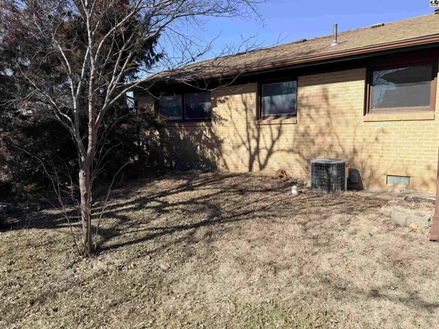Brick exterior wall with windows, an air conditioning unit, and a bare yard.