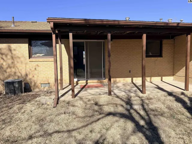 Covered patio with wood posts extends from a brick house with a sliding glass door.