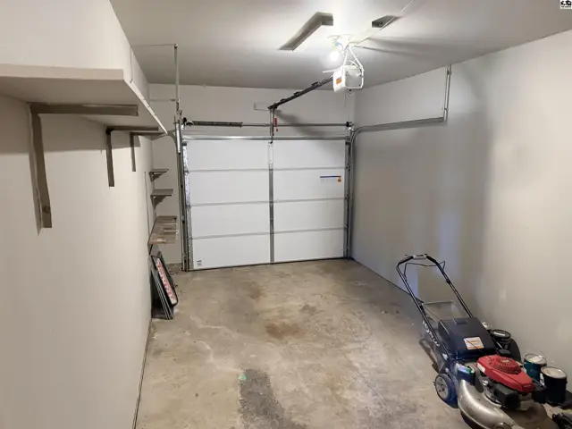 This attached garage features a white sectional door, concrete floor, and wall-mounted shelving.