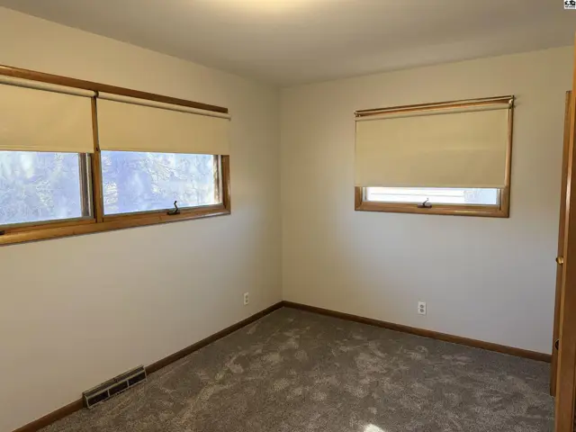 Carpeted room with two windows and a heating vent.