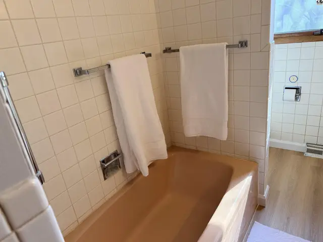 This bathroom features a tan bathtub, white tiled walls, and chrome towel bars.