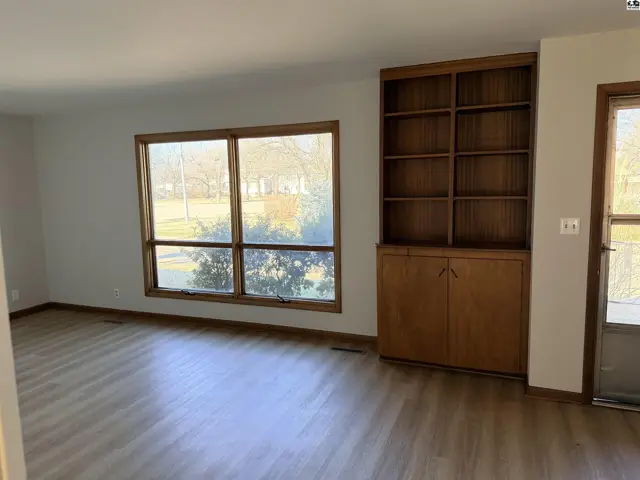 Spacious living area features a large window and built-in wooden shelving unit.