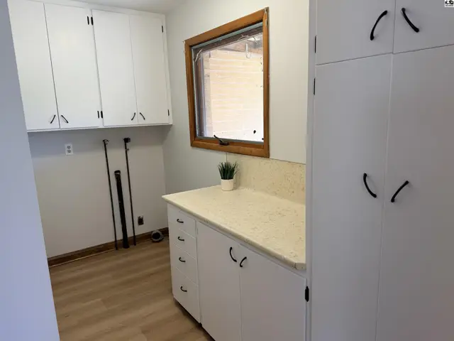White cabinetry, a speckled countertop, and a wood-trimmed window accent this laundry room.