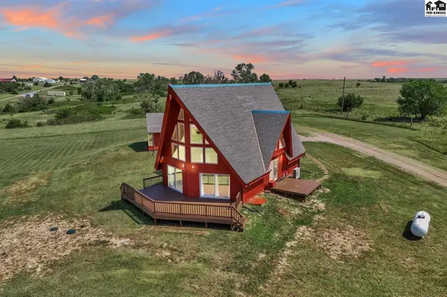 A-frame home with red siding, expansive windows, and a large wooden deck in a rural setting.