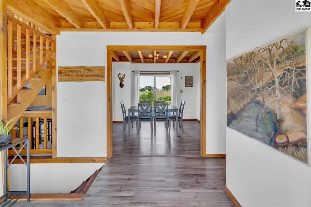 Rustic wooden beams accent a dining room with a table and chairs, visible through an archway.