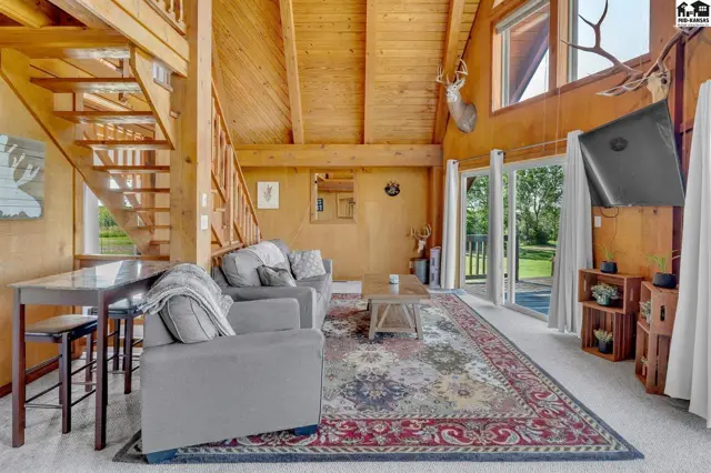 Cozy living room with vaulted wood ceilings, a stone fireplace, and large windows overlooking the outdoors.