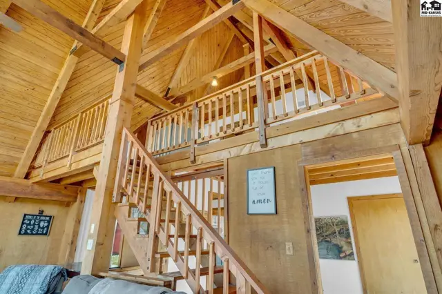 Spacious interior with exposed wooden beams, a lofted balcony, and a wooden staircase.