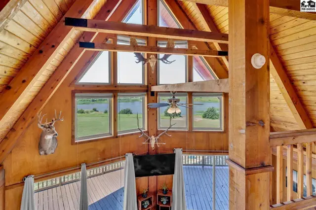 Rustic great room with exposed wood beams, vaulted ceiling, large windows, and mounted deer heads.