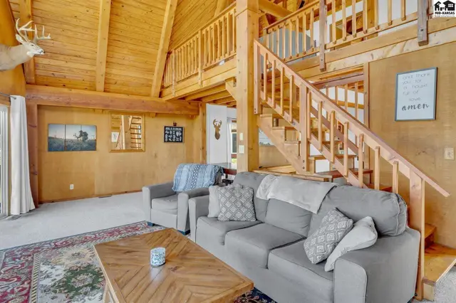 Spacious living room with vaulted wood ceilings, exposed beams, and a prominent wooden staircase.