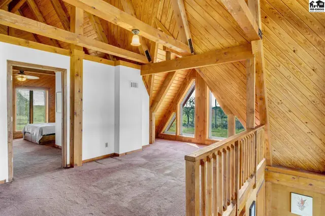 Loft area with vaulted wood ceilings, exposed beams, and a view into a bedroom.