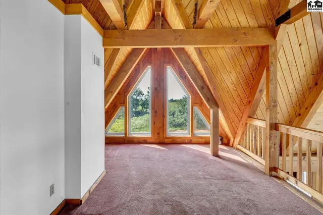 Attic loft with vaulted wood ceilings, exposed beams, and unique triangular windows overlooking greenery.