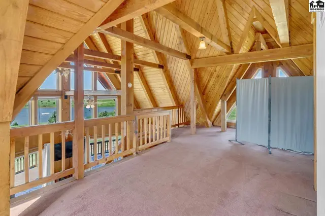 Spacious loft with exposed wooden beams, vaulted ceilings, and a railing overlooking a scenic view.