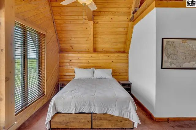 Cozy bedroom with wood-paneled walls and ceiling, a large window, and a framed map.