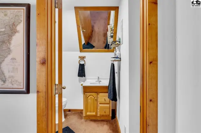 Compact bathroom with wood vanity, white sink, large mirror, and a toilet, framed by natural wood trim.