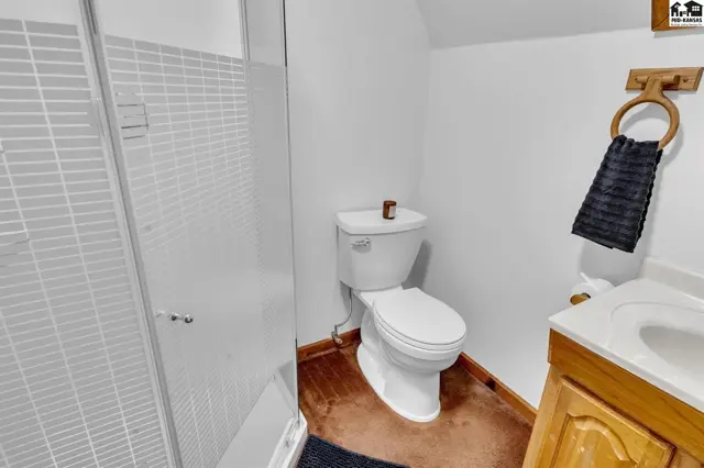 White toilet and tiled shower stall in a bathroom with wood vanity and dark flooring.