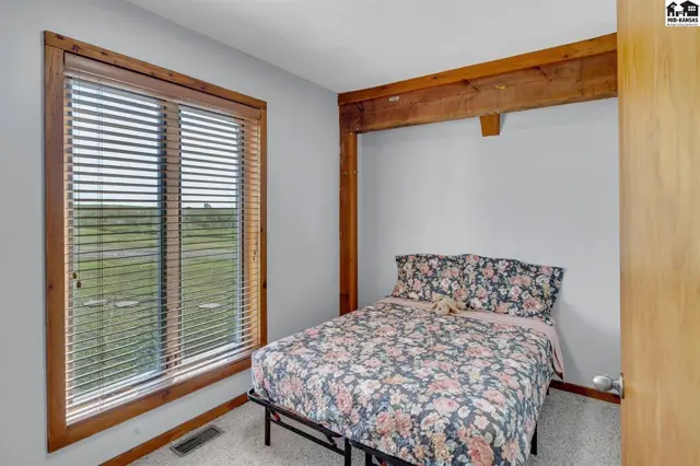Cozy bedroom with floral bedding, large window, and rustic wood beam accent.