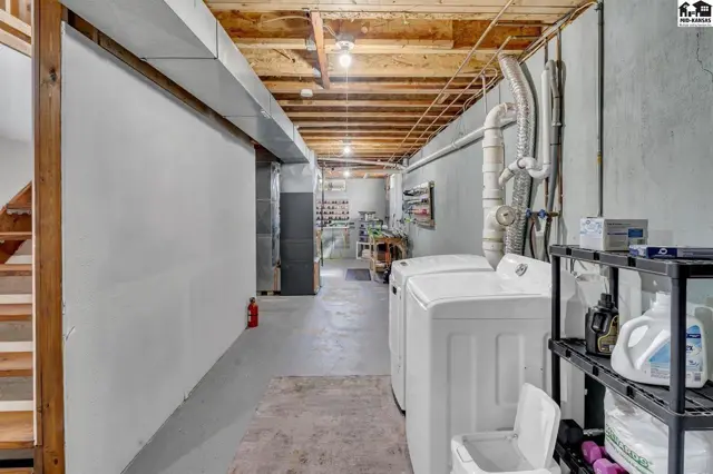 Unfinished basement with laundry machines, exposed wood joists, and concrete floors.