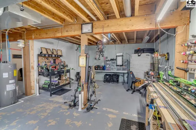 Finished basement workshop with exposed beams, storage shelves, and archery equipment.