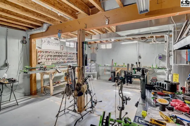 Finished basement workshop with exposed beams, workbenches, and archery equipment.