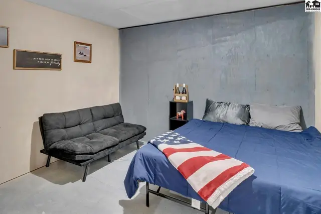 Bedroom with a blue bed, American flag throw, black futon, and textured gray wall.