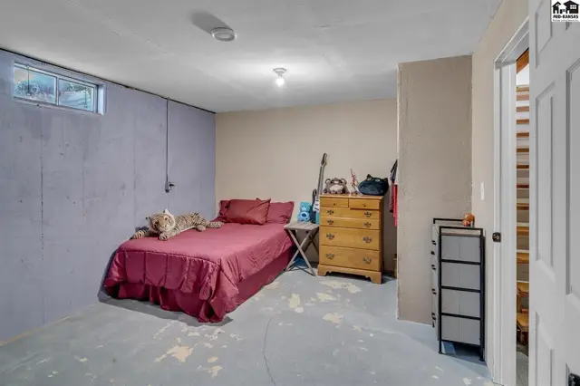 Unfinished basement bedroom with concrete floor, purple accent wall, and wooden dresser.