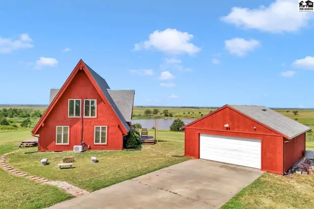 Red A-frame house and detached garage sit on a grassy lot with a pond in the distance.