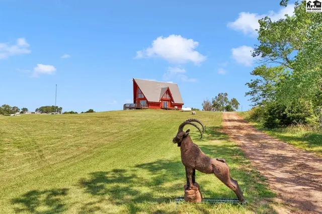 Red A-frame house on a grassy hill with a metal ibex statue in the foreground.