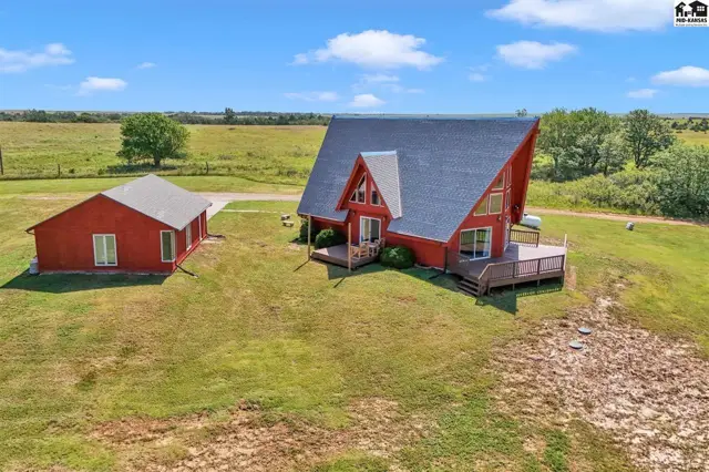 Red A-frame house with a large deck and detached garage sits on a grassy knoll.