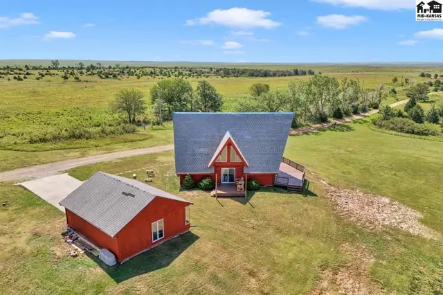 Red A-frame house with a detached garage sits on a vast, open grassy landscape under a blue sky.