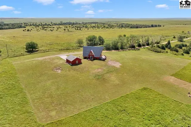 Sprawling rural property features a red-roofed home and outbuilding amidst vast, open fields.