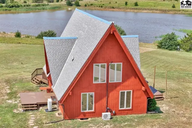 A-frame house with red siding, white trim windows, and a deck, set beside a tranquil lake.