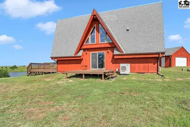Red A-frame home with large deck and adjacent garage on a grassy lot.