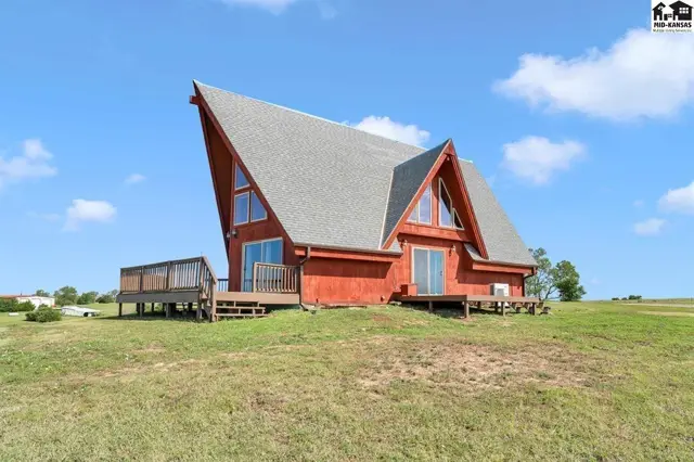 Unique red A-frame home with a large deck and expansive windows under a blue sky.