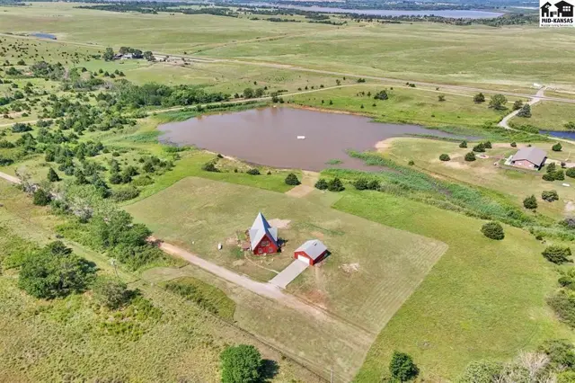 Aerial view of a red barn and outbuilding on a grassy lot beside a large pond.