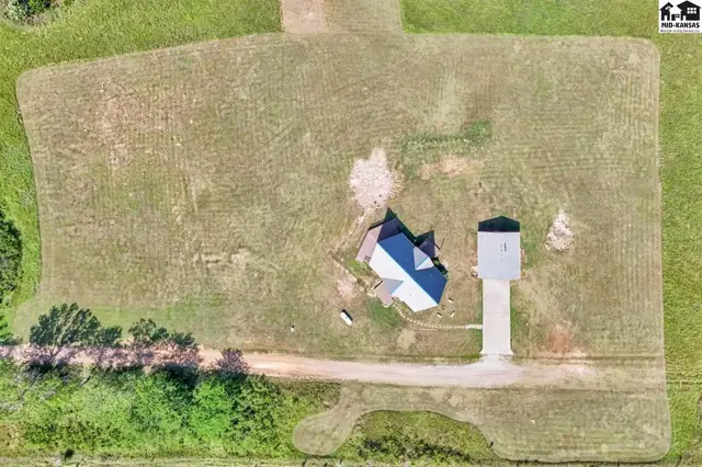 Aerial view of a single-story home with a dark roof, surrounded by a large, mowed yard.