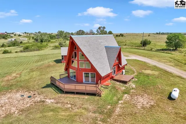 Red A-frame house with large windows and wooden decks sits on a grassy hillside.